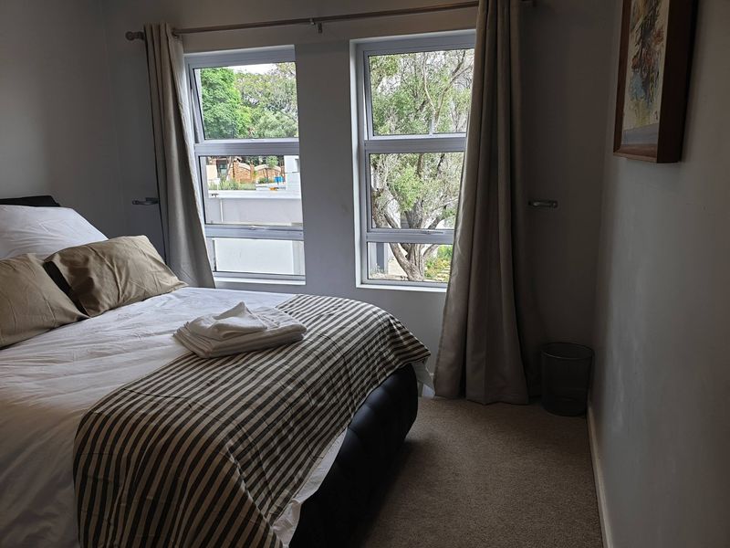 A well-lit bedroom featuring neutral carpeting and dual aluminium-framed windows with views of the surrounding greenery.
