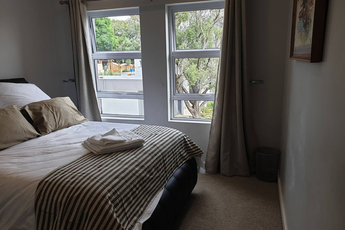 A well-lit bedroom featuring neutral carpeting and dual aluminium-framed windows with views of the surrounding greenery.