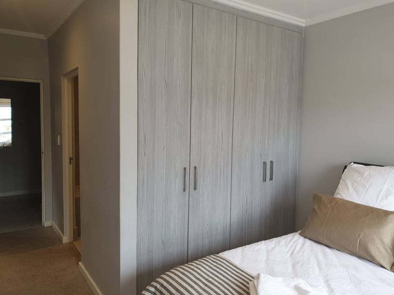 A bedroom featuring modern grey wood-grain built-in cupboards and neutral wall finishes, with an adjacent doorway leading to an internal space.
