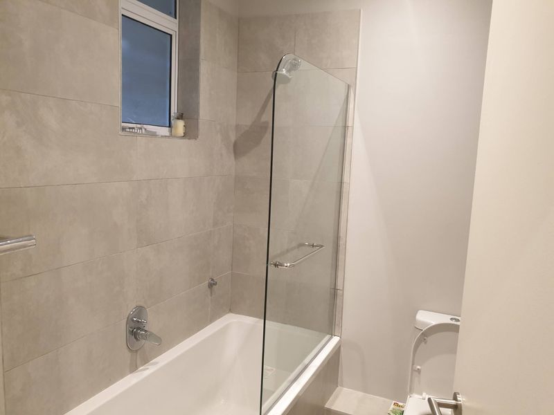 A modern bathroom featuring a bathtub with a glass shower screen, tiled walls, and a standard toilet.