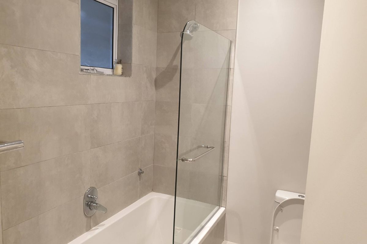 A modern bathroom featuring a bathtub with a glass shower screen, tiled walls, and a standard toilet.