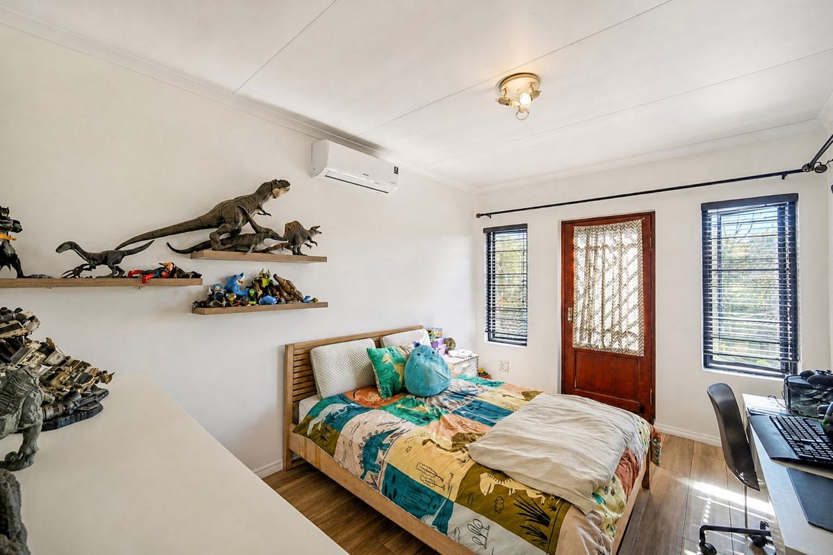 A well-lit bedroom featuring laminate flooring, an air conditioning unit, and direct access to an outdoor area through a wooden door.