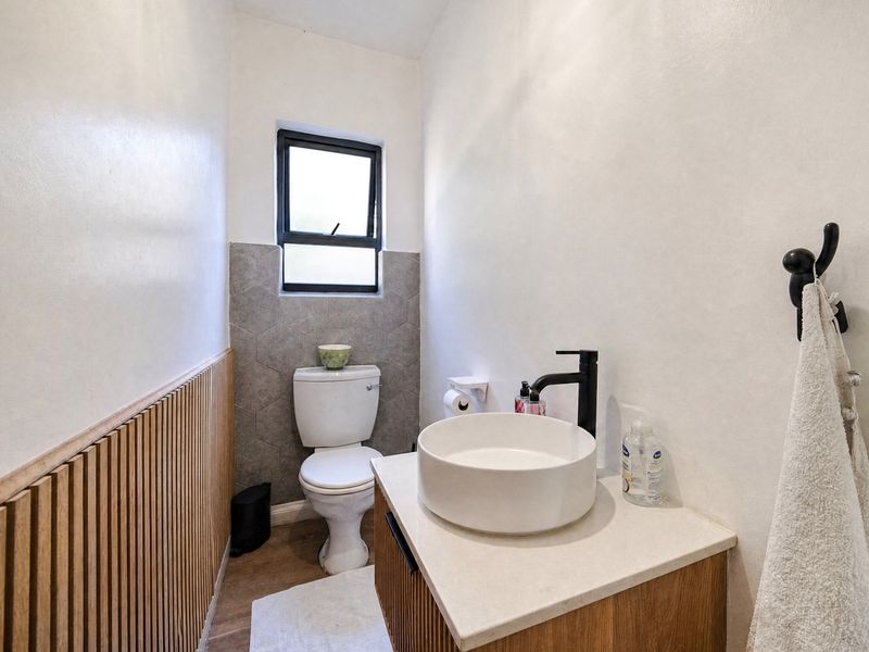 A modern guest bathroom featuring a timber slat feature wall, hexagonal tile backsplash, vessel sink on a stone vanity, and contemporary black fixtures.
