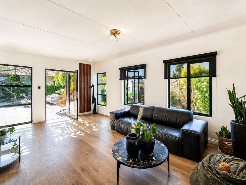 Bright living room featuring timber flooring, modern black-framed windows, and direct access to an outdoor patio area.