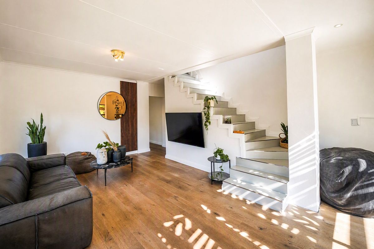 A bright living room featuring timber flooring, a modern staircase, and a wall-mounted television, creating a clean and contemporary living space.
