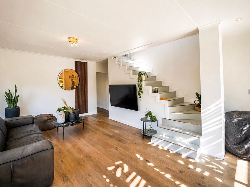 A bright living room featuring timber flooring, a modern staircase, and a wall-mounted television, creating a clean and contemporary living space.