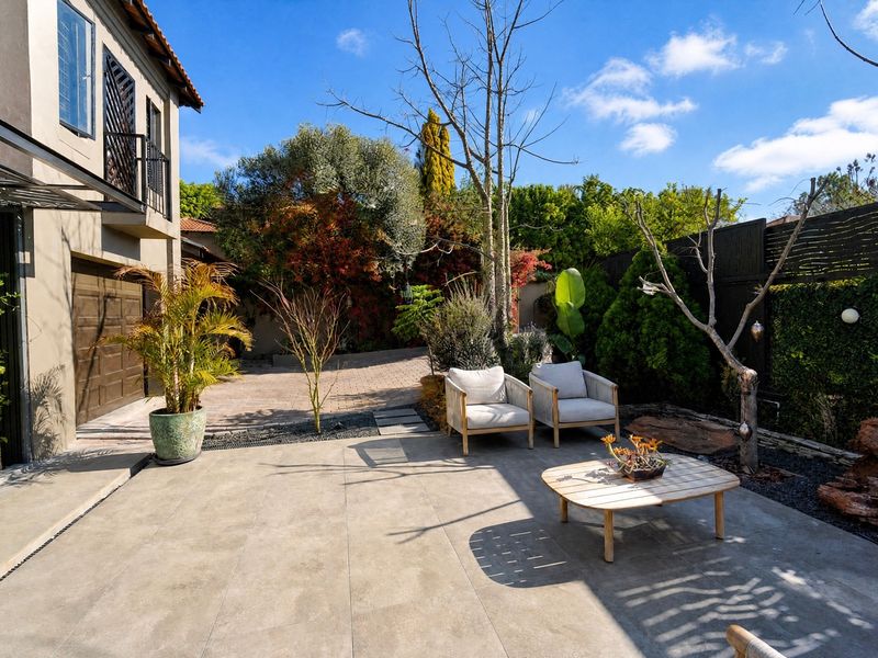 A well-maintained rear exterior featuring a tiled patio area, paved driveway, and access to the garage, complemented by established garden landscaping.