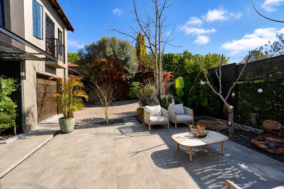 A well-maintained rear exterior featuring a tiled patio area, paved driveway, and access to the garage, complemented by established garden landscaping.