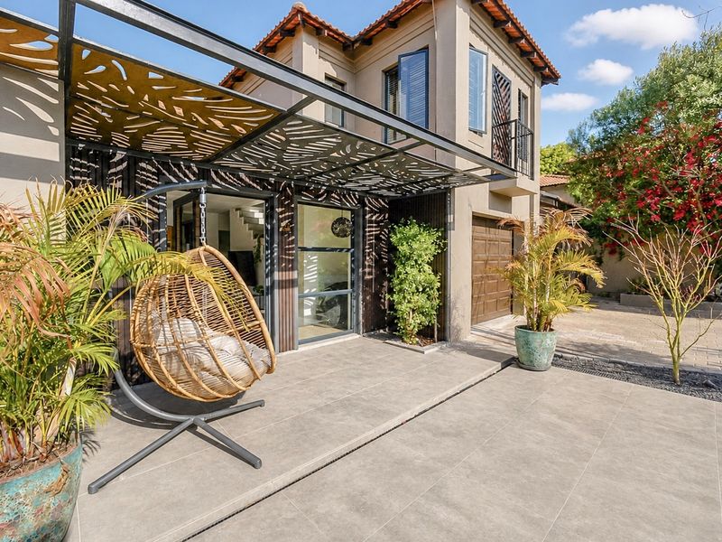 A modern covered patio area featuring decorative laser-cut metal roofing, tiled flooring, and seamless access to the main residence and garage.