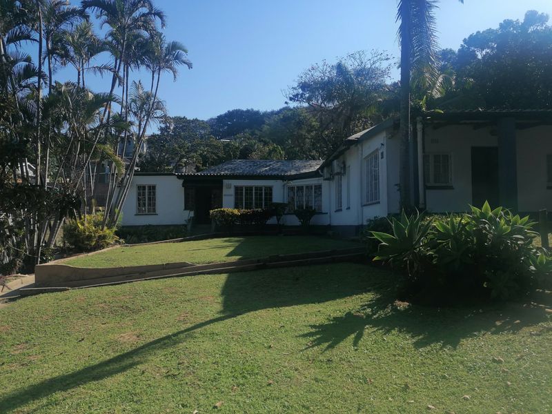 Front elevation of a single-story residential house featuring a tiled roof, casement windows, and a surrounding garden with a concrete retaining wall.