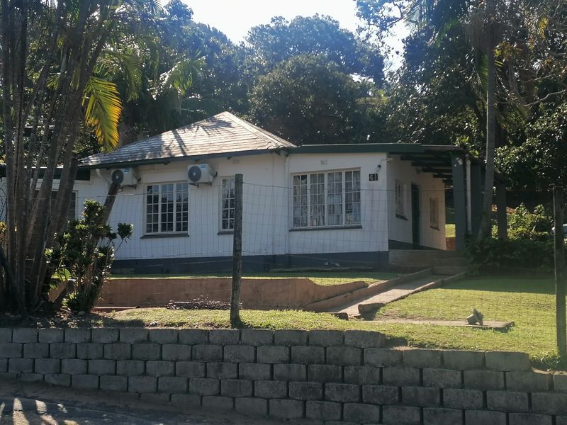 Front elevation of a single-story house featuring a hip roof, casement windows, and an established garden with a concrete retaining wall.