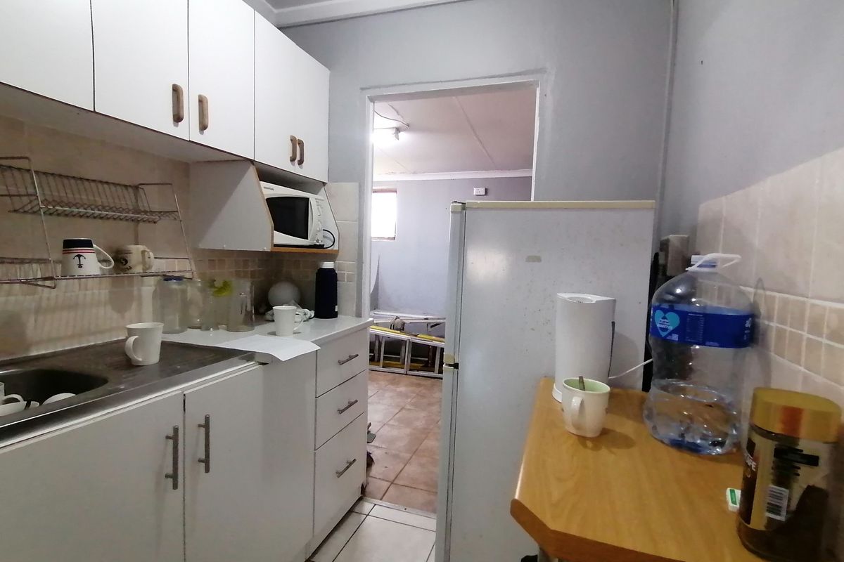 A compact kitchen featuring white built-in cabinetry, tiled backsplash, and tiled flooring, providing a functional prep area with direct access to an adjacent room.