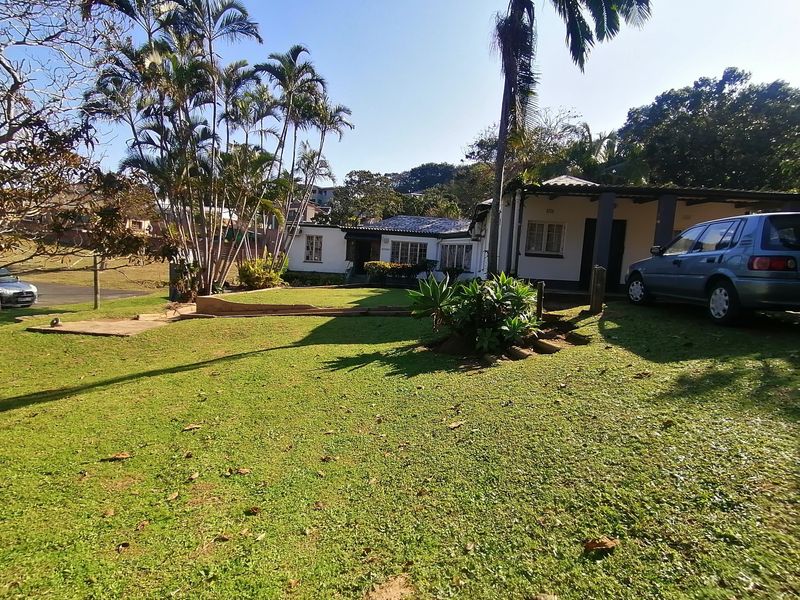 Front view of the house featuring a spacious lawn, established garden, and a covered patio area with a concrete driveway.