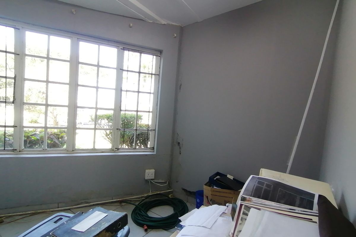 A vacant bedroom featuring tiled flooring and a large grid-pattern window, requiring cosmetic updates to the walls and finishes.