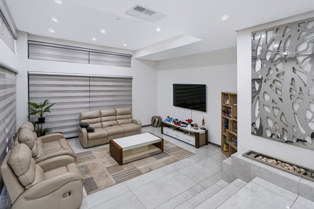 A modern, well-lit living room featuring tiled flooring, recessed downlighting, ducted air conditioning, and a contemporary built-in fireplace.