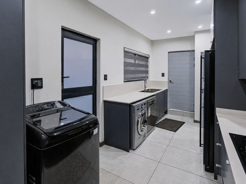 Modern, well-appointed laundry room featuring sleek dark cabinetry, stone countertops, integrated sink, and tiled flooring with direct exterior access.