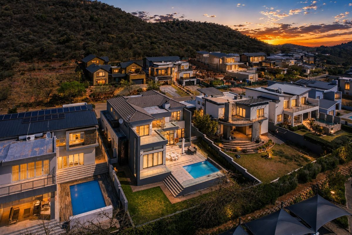 An elevated aerial view of a modern residential estate at sunset, showcasing contemporary homes with swimming pools, balconies, and integrated solar energy systems.