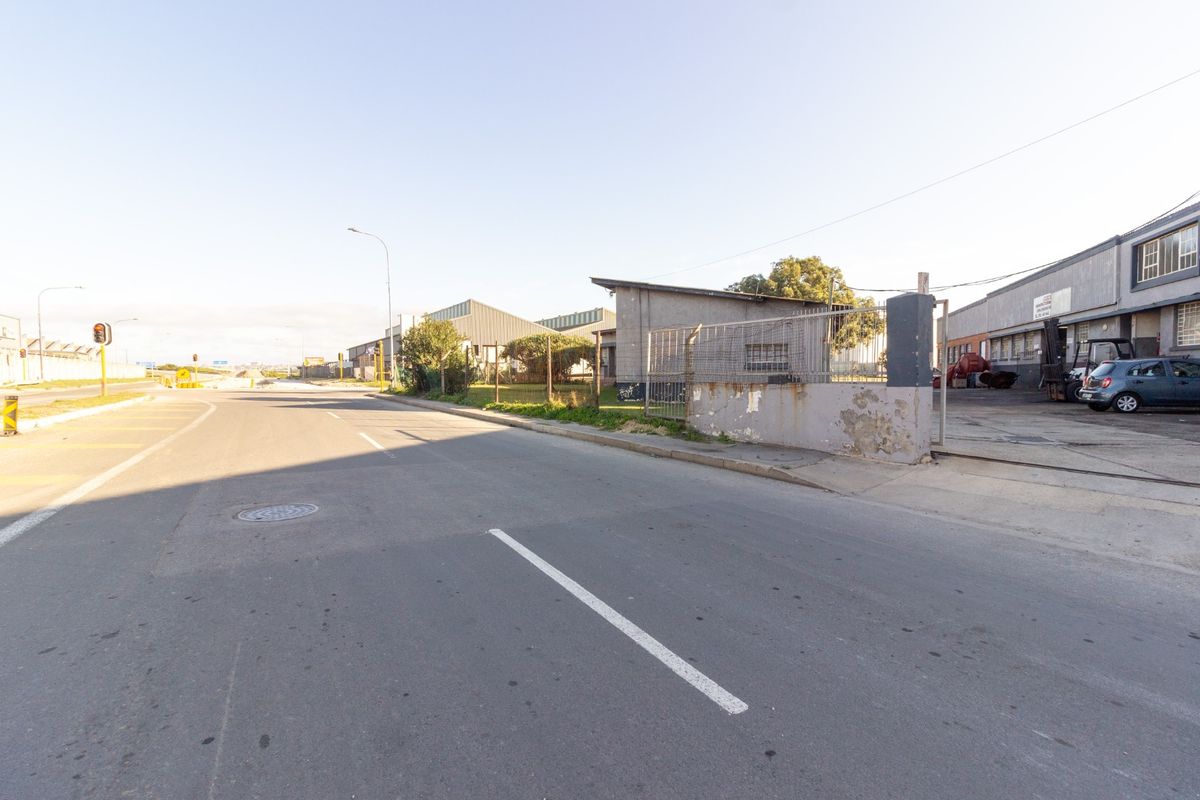 Street view of an industrial property featuring a concrete boundary wall, metal fencing, and access to the warehouse facility.