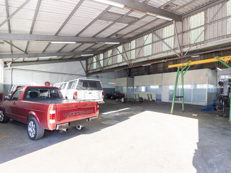 Spacious industrial garage featuring high ceilings with exposed steel trusses, concrete flooring, integrated lighting, and a built-in gantry crane for heavy-duty operations.