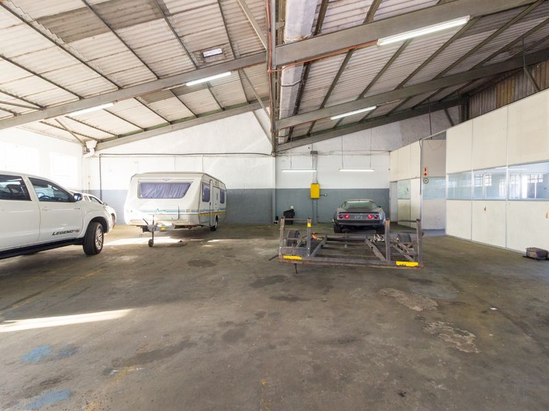 Spacious industrial garage featuring exposed steel roof trusses, fluorescent lighting, and a partitioned office area, suitable for storage or workshop use.