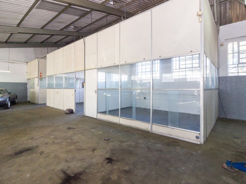 Industrial warehouse space featuring a partitioned office structure with glass paneling, exposed steel roof trusses, and durable concrete flooring.