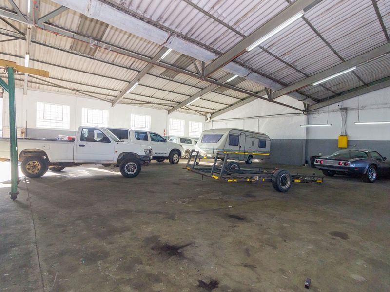 Spacious industrial garage featuring high ceilings with exposed steel trusses, fluorescent lighting, and durable concrete flooring, suitable for vehicle storage or workshop use.