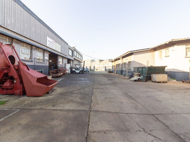 Industrial yard area featuring concrete paving and access to warehouse units with metal cladding and steel-framed windows.