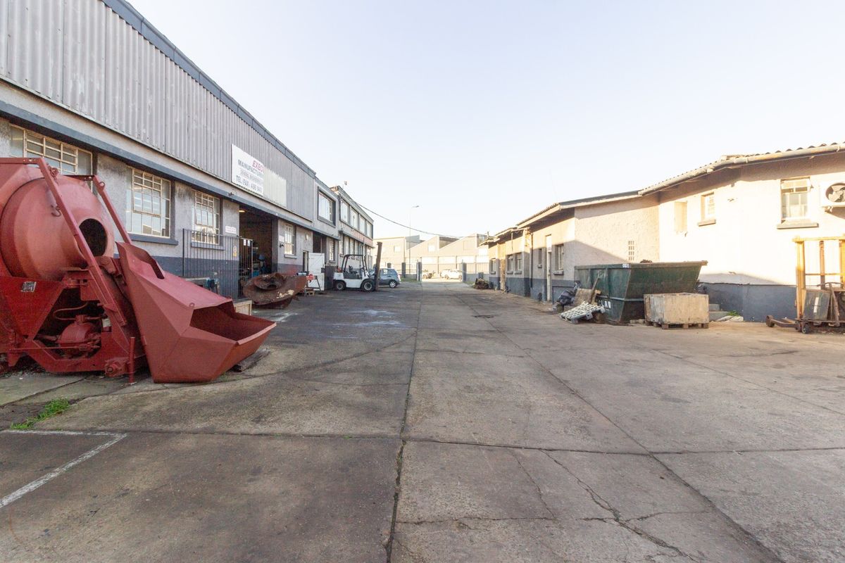 Industrial yard area featuring concrete paving and access to warehouse units with metal cladding and steel-framed windows.