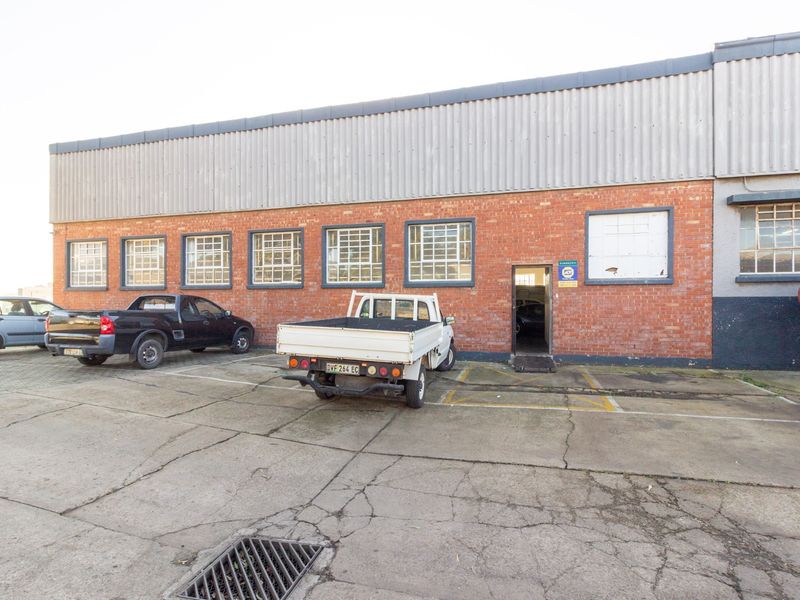 Exterior view of an industrial warehouse building featuring a brick facade, corrugated metal upper cladding, and a concrete parking area.