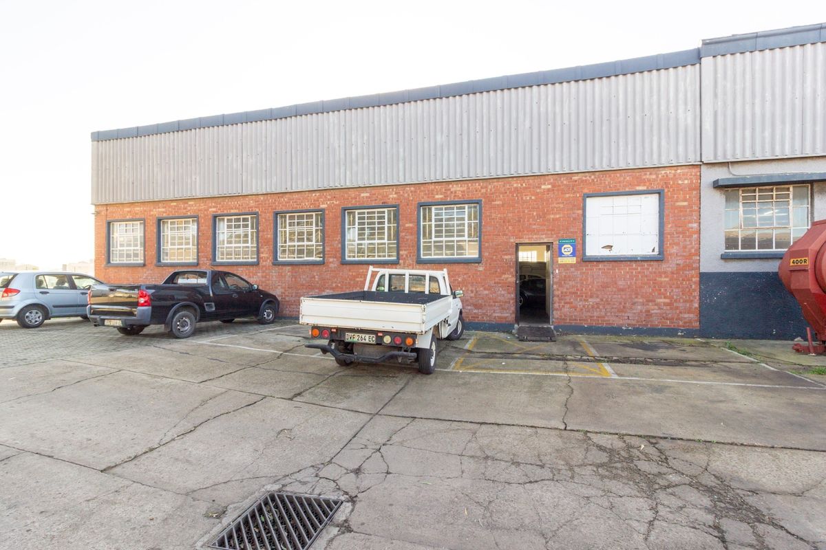 Exterior view of an industrial warehouse building featuring a brick facade, corrugated metal upper cladding, and a concrete parking area.