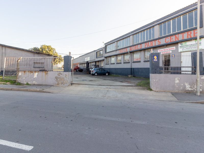 Front exterior view of an industrial truck parts facility featuring a concrete driveway, perimeter security wall, and multi-level industrial building facade.