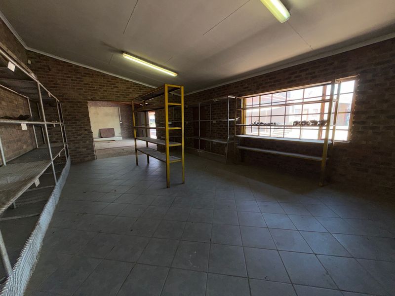 An industrial utility space featuring exposed brick walls, tiled flooring, and fixed metal shelving units, suitable for storage or workshop use.