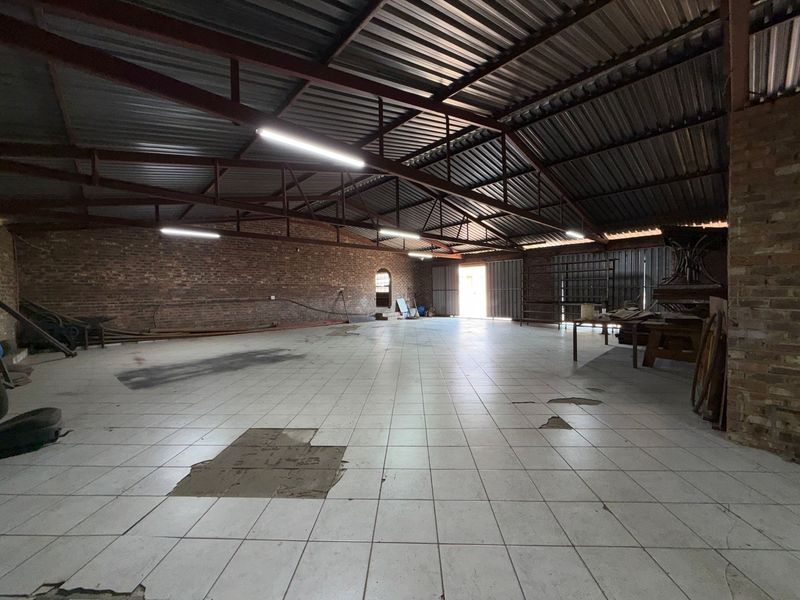 Spacious industrial utility area featuring exposed steel roof trusses, brick walls, and tiled flooring, suitable for storage or workshop use.