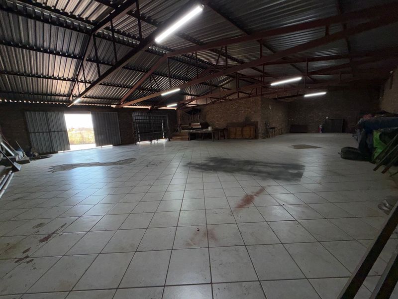 Spacious industrial utility area featuring exposed steel roof trusses, tiled flooring, and large sliding doors, suitable for workshop or storage use.