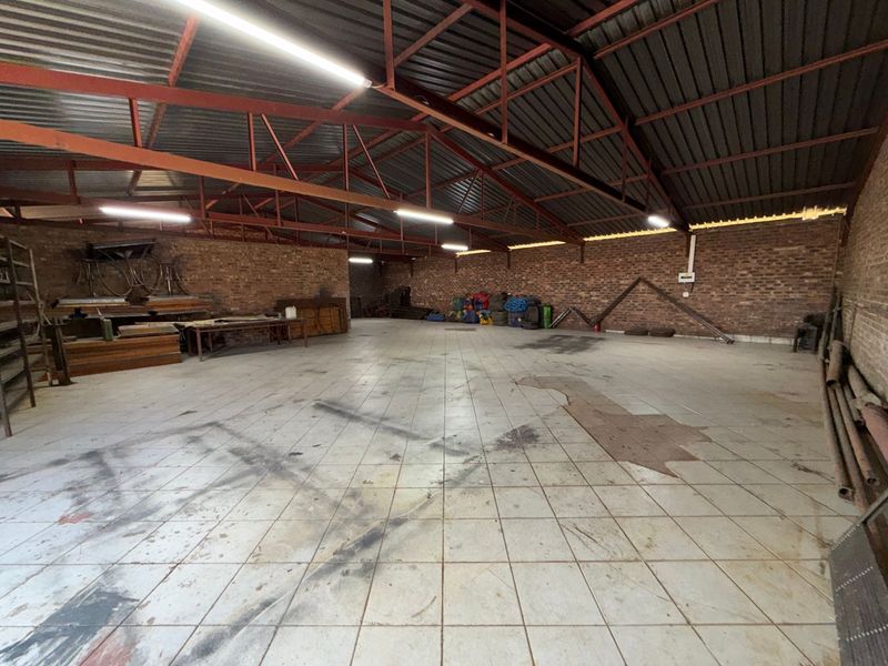 Spacious industrial utility area featuring exposed steel roof trusses, brick walls, and tiled flooring, suitable for storage or workshop use.