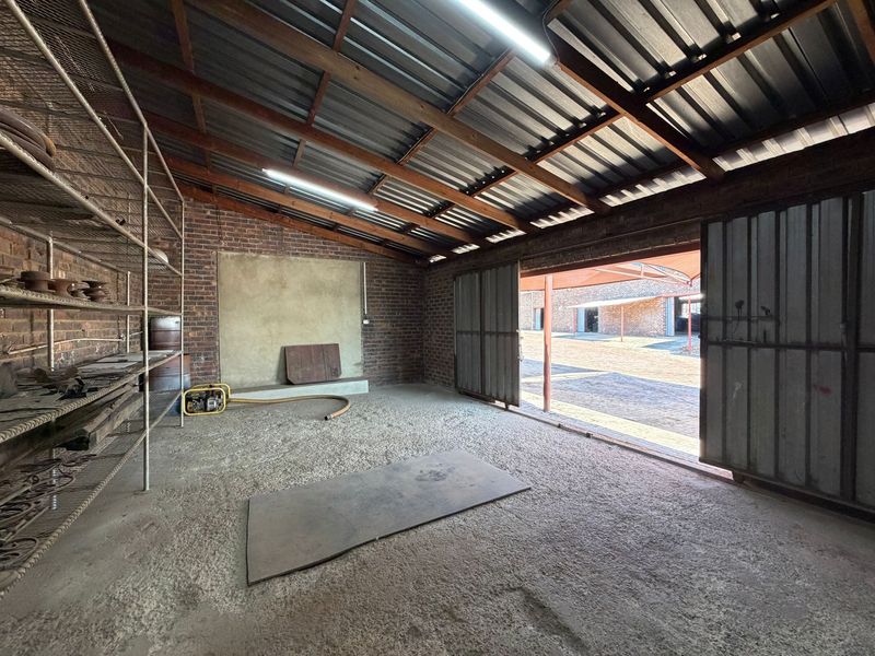 A spacious industrial utility area featuring exposed brick walls, corrugated metal roofing, and large sliding doors opening to an outdoor yard.