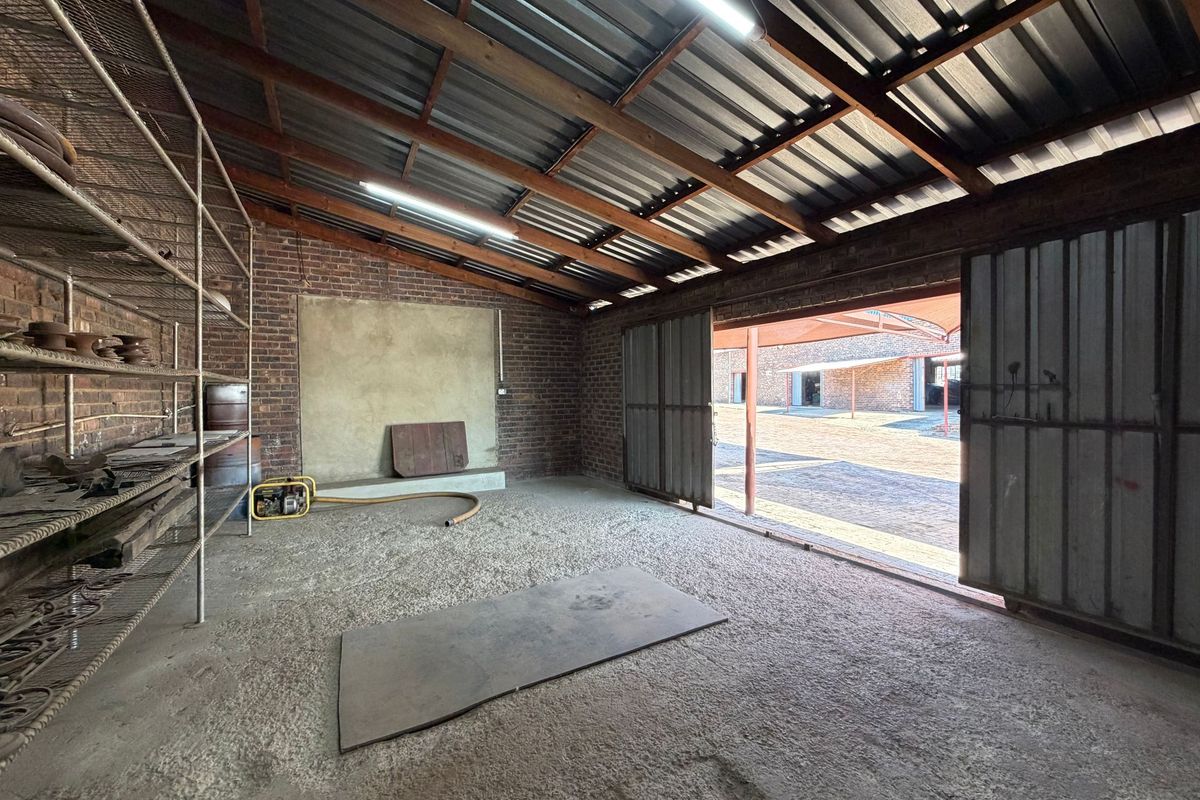 A spacious industrial utility area featuring exposed brick walls, corrugated metal roofing, and large sliding doors opening to an outdoor yard.