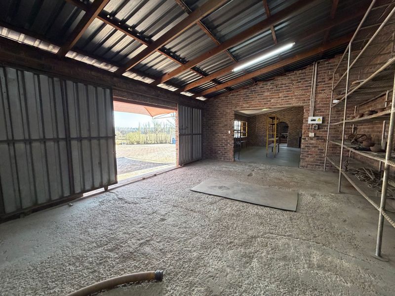 Spacious industrial utility area featuring exposed brick walls, timber roof trusses, concrete flooring, and large sliding metal doors opening to the exterior.