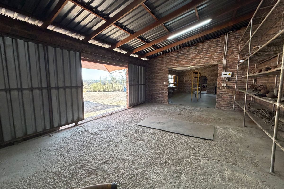 Spacious industrial utility area featuring exposed brick walls, timber roof trusses, concrete flooring, and large sliding metal doors opening to the exterior.