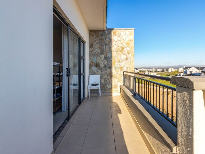 A spacious balcony featuring tiled flooring, a stone-clad feature wall, and a metal balustrade, offering clear views of the surrounding estate.
