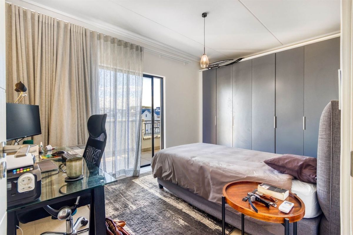 A well-lit bedroom featuring built-in cupboards, tiled flooring, and a sliding glass door providing access to a balcony.