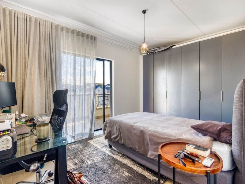 A well-lit bedroom featuring built-in cupboards, tiled flooring, and a sliding glass door providing access to a balcony.