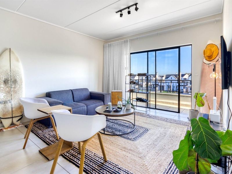 A bright living room featuring tiled floors, track lighting, and a large sliding glass door providing access to a balcony with neighborhood views.