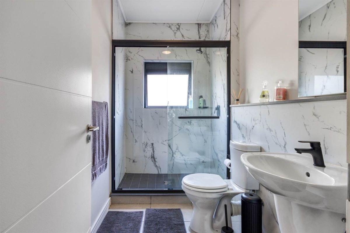 Modern bathroom featuring marble-look wall tiles, a walk-in shower with black frame, pedestal basin, and contemporary black tapware.