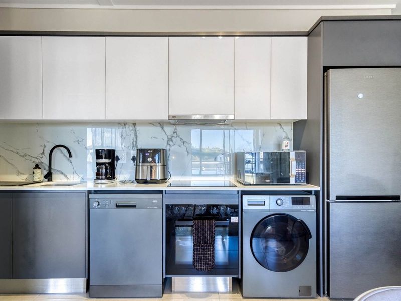 Modern kitchen featuring sleek white and grey cabinetry, marble-look splashback, integrated appliances, and high-quality finishes throughout.