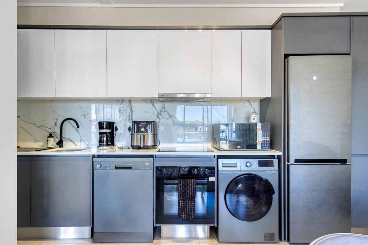 Modern kitchen featuring sleek white and grey cabinetry, marble-look splashback, integrated appliances, and high-quality finishes throughout.