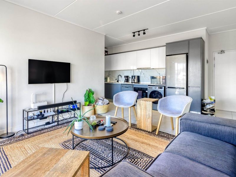 Modern open-plan living area featuring a sleek kitchen with integrated appliances, marble-look splashback, and contemporary track lighting, seamlessly flowing into the lounge space.