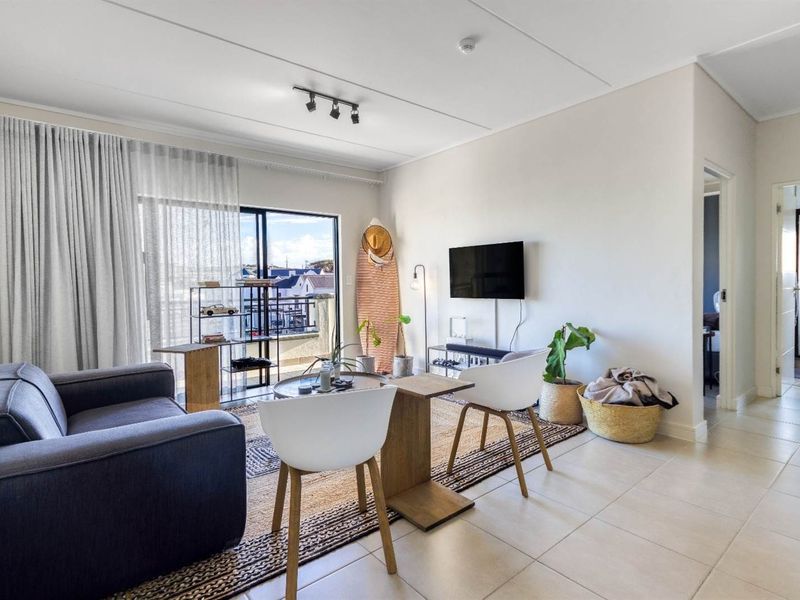 A bright living room featuring tiled flooring, track lighting, and a large sliding glass door providing access to an outdoor balcony area.