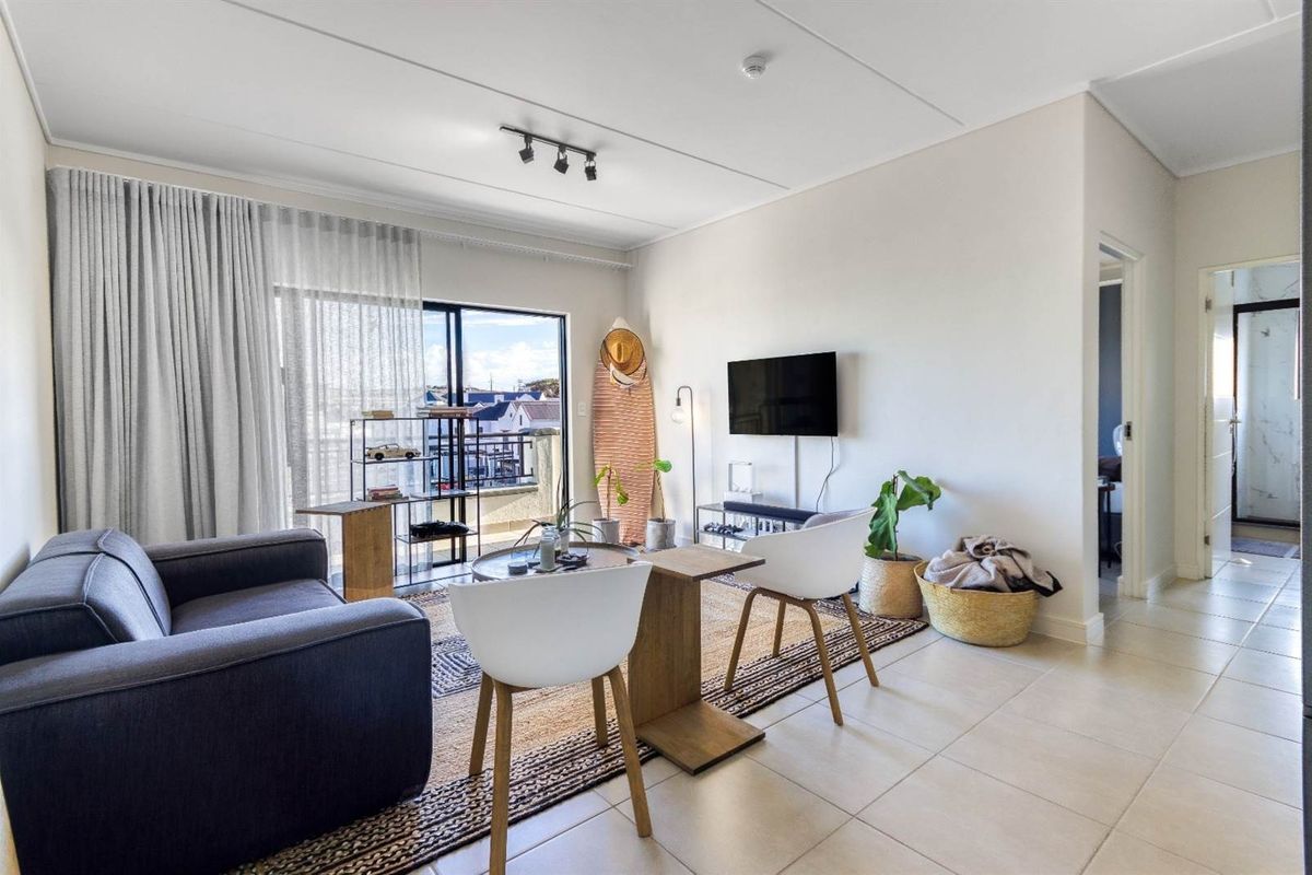 A bright living room featuring tiled flooring, track lighting, and a large sliding glass door providing access to an outdoor balcony area.