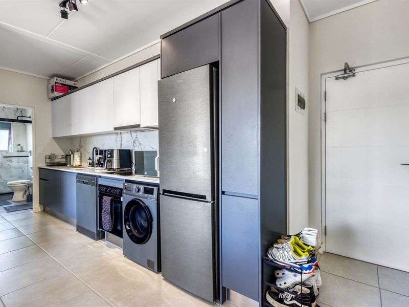 Modern kitchen featuring sleek two-tone cabinetry, marble-look splashback, integrated appliances, and tiled flooring, with an adjacent view into the bathroom.